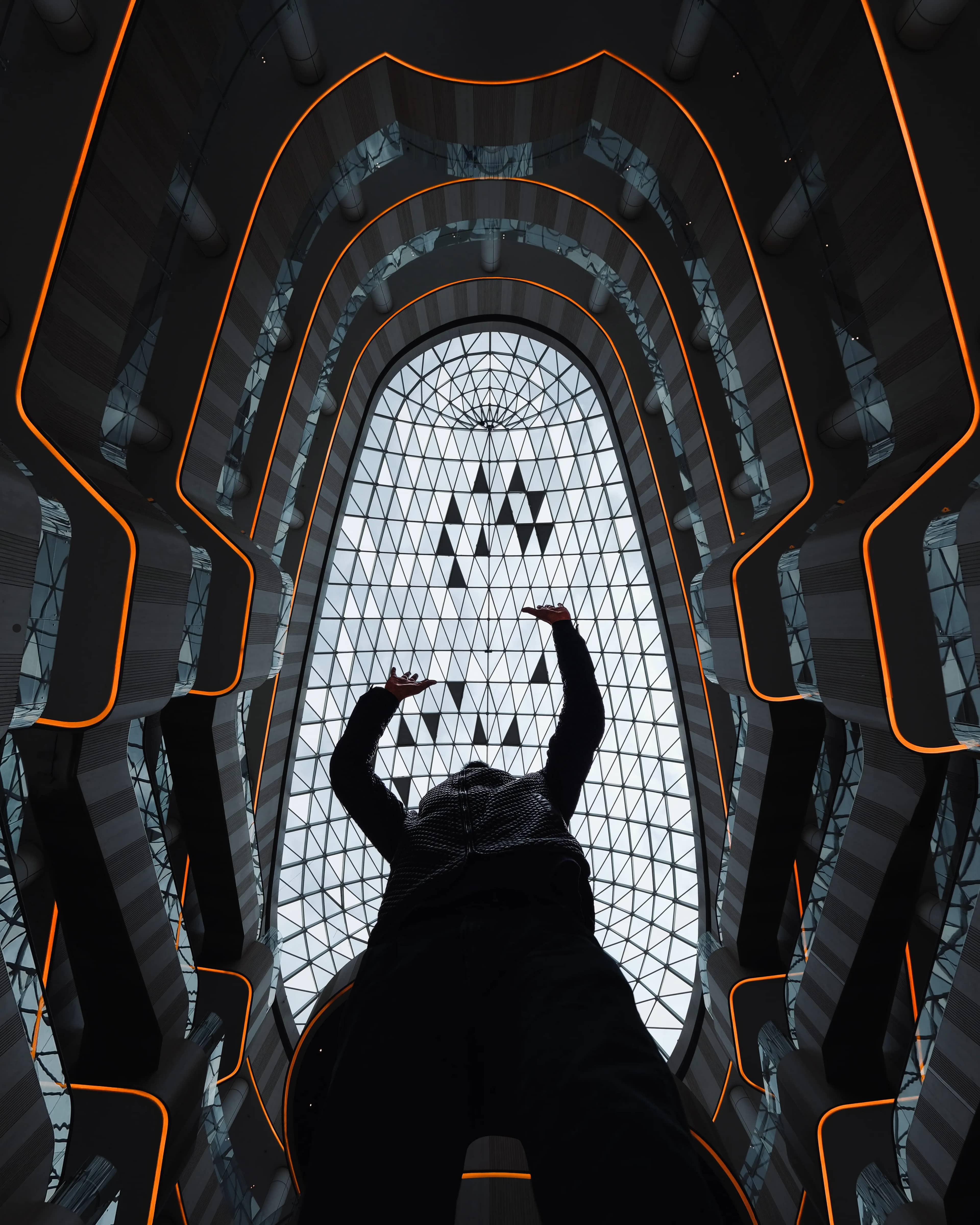 A figure viewed from below inside an atrium traced with orange light.